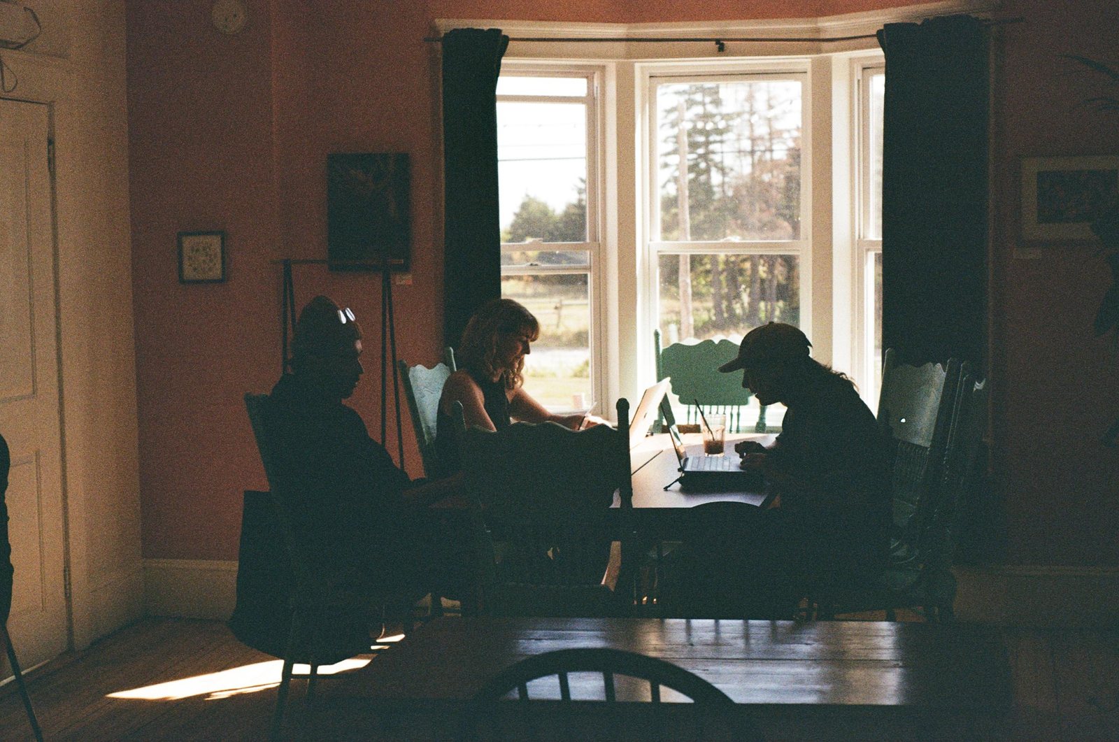Three people gathered around a table in warm window light