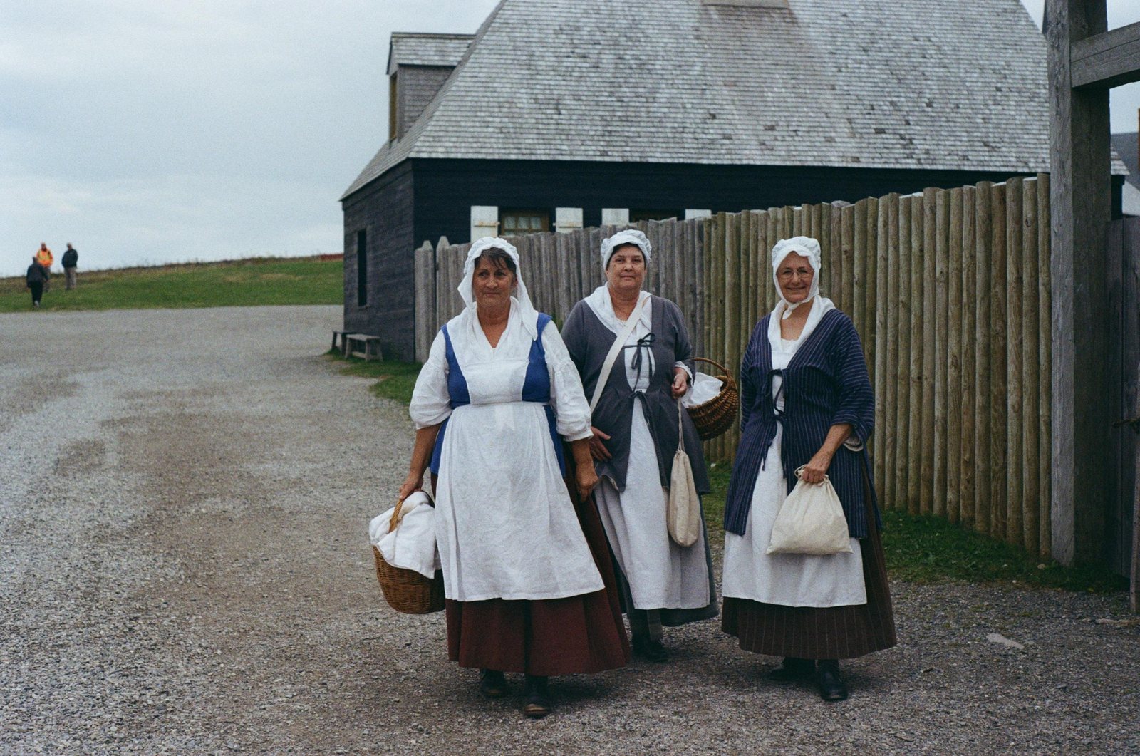 Three women in historic dress standing outside a wooden fort