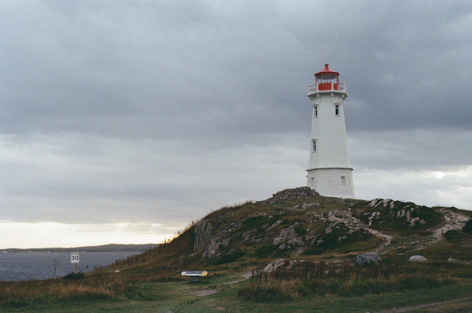 A white lighthouse with a red roof beneath dark clouds