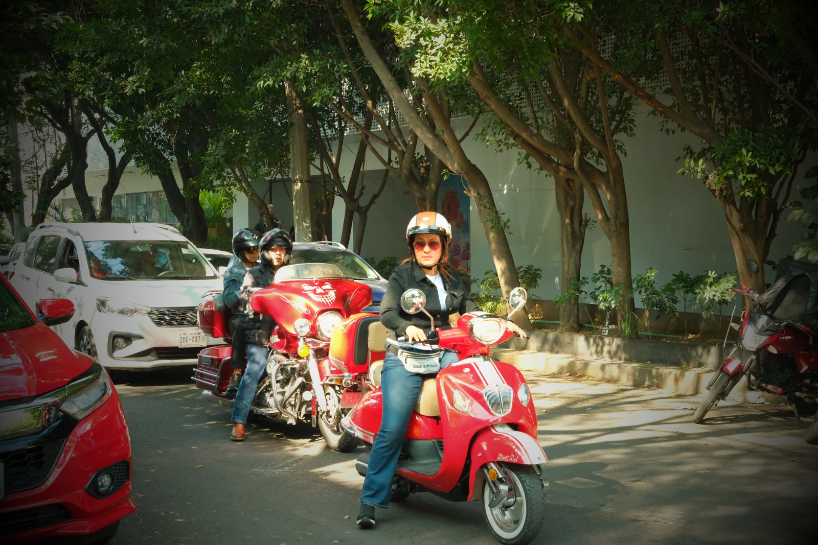 A rider on a red scooter along a tree-lined street