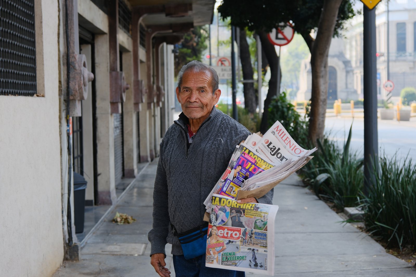 A newspaper seller standing on a shaded sidewalk